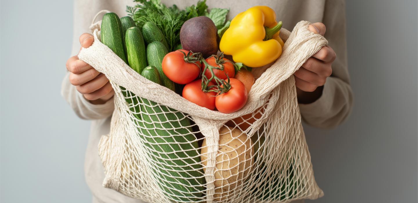 Hands holding reusable mesh bag filled with fresh vegetables