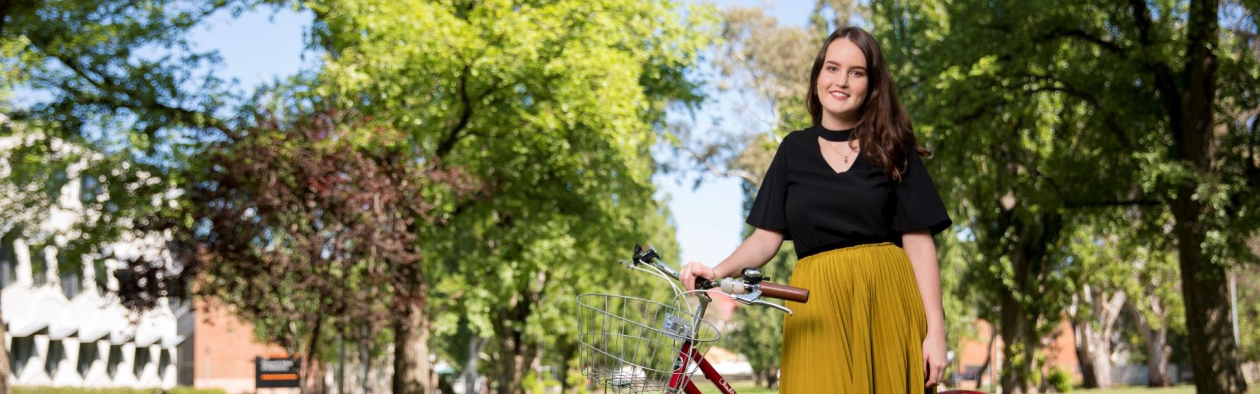 Image of women standing in front of bicycle with grass and trees as background