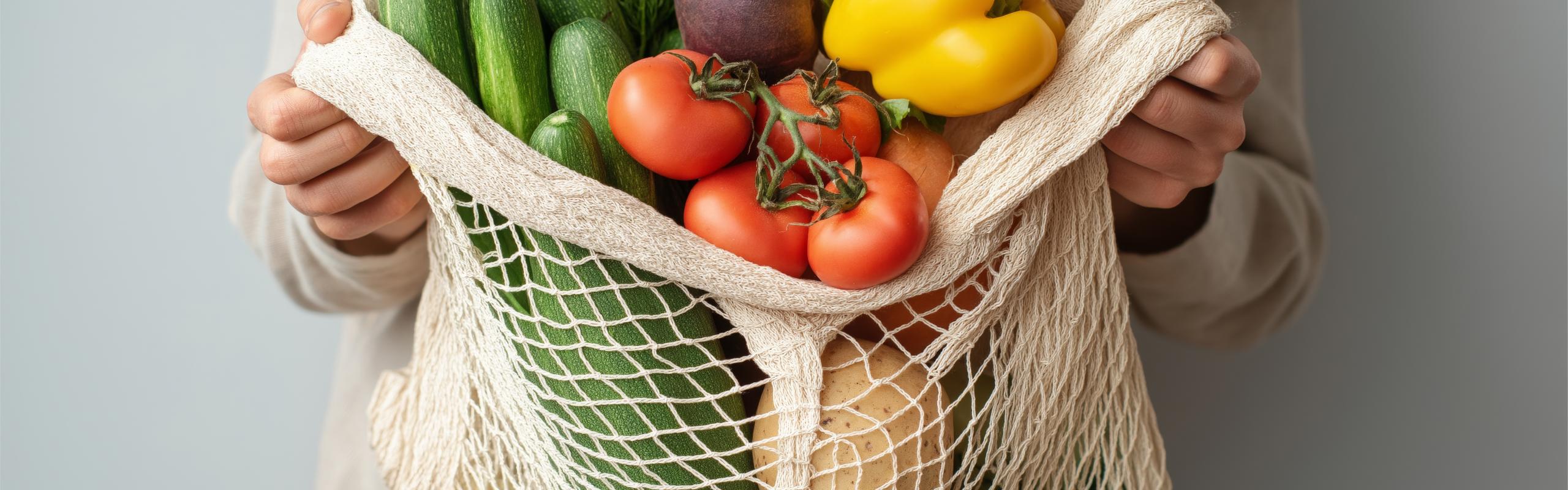 Hands holding reusable mesh bag filled with fresh vegetables